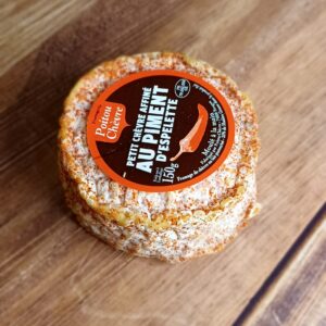 Vue en plongée d'un fromage rond, partiellement enrobé de piment d'espelette. Une étiquette ronde sur le dessus du fromage indique le nom "Chèvre au Piment d'Espelette"