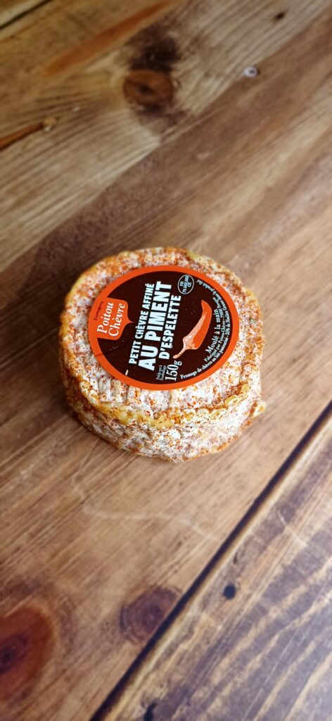 Vue en plongée d'un fromage rond, partiellement enrobé de piment d'espelette. Une étiquette ronde sur le dessus du fromage indique le nom "Chèvre au Piment d'Espelette"
