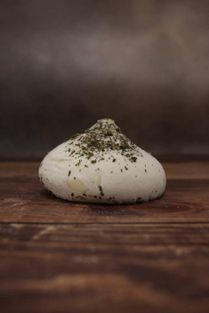 Photo de face d'un fromage en forme de meringue blanche, saupoudré de basilic.